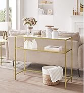 à cadre doré avec deux étagères en verre derrière un canapé beige. La table présente des objets de décoration, notamment des vases, des bougies et des livres, dans un salon lumineux.