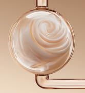 Photographie de produit en gros plan montrant des surfaces incurvées, brillantes en or rose ou cuivré avec des lignes lisses et fluides sur fond beige.