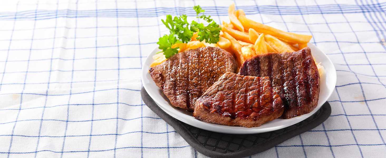 Assiette avec bifteck grillé, frites et garniture sur une nappe à carreaux bleus et blancs. La viande présente des marques de cuisson distinctes.