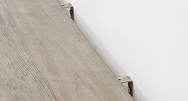 Gros plan d'un revêtement de sol ou de lambris à texture de bois clair avec des clips métalliques visibles le long du bord, ce qui suggère un