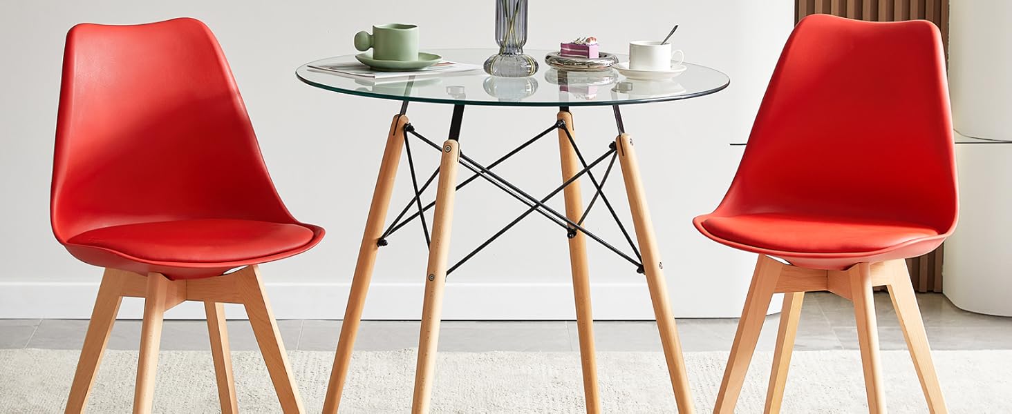 avec table ronde en verre et deux chaises en plastique moulé rouge avec pieds en bois. Panneaux muraux décoratifs et étagères en arrière-plan.