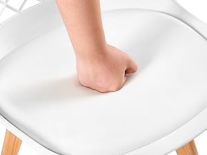 Gros plan d'un siège de chaise blanc avec un poing enfoncé sur sa surface, démontrant ainsi son amorti ou sa douceur. Pieds de chaise en bois visibles à l'arrière-plan.