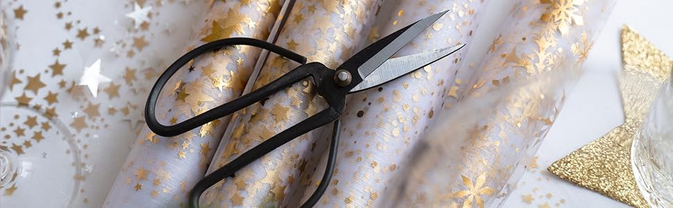 Ciseaux à tissu posés sur un tissu à motifs scintillants ou métalliques avec des éléments de design décoratifs visibles.