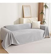 gris clair aux bords à pompons, posé sur un canapé dans un décor de salon minimaliste avec des coussins décoratifs