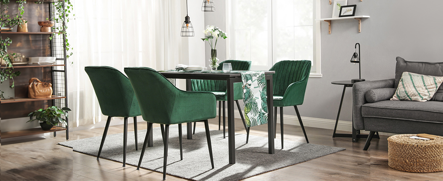 avec table rectangulaire en bois et quatre chaises en velours vert. La décoration environnante comprend des plantes, des étagères et un canapé gris
