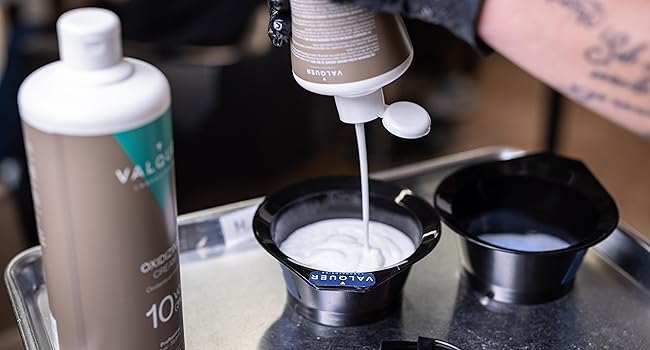 Procédé de coloration des cheveux montrant que le révélateur de crème est distribué dans des bols à mélanger noirs. La bouteille étiquetée « 10 » est visible en arrière-plan, avec la marque « Valo » partiellement visible