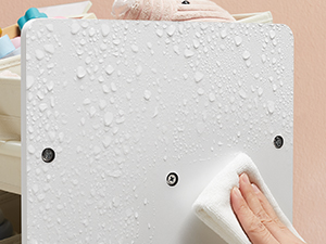 Essuyer à la main une surface texturée blanche avec des gouttelettes d'eau, pour démontrer le nettoyage ou l'entretien de ce qui semble être un mur ou un panneau