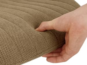 Gros plan d'une main appuyant sur une housse de coussin en tissu beige texturé, démontrant sa douceur et son élasticité. Le tissu semble être un tissu tricoté extensible avec un motif côtelé