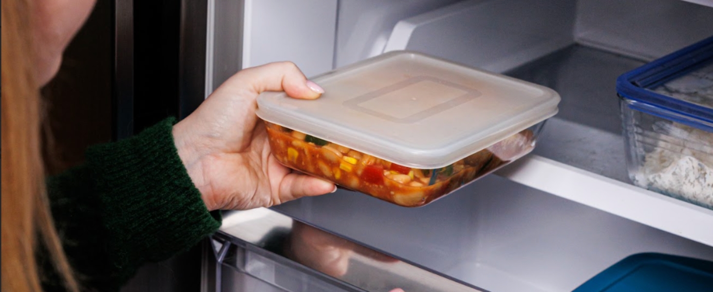 Placer à la main un contenant alimentaire en plastique transparent contenant du contenu orange dans un réfrigérateur.